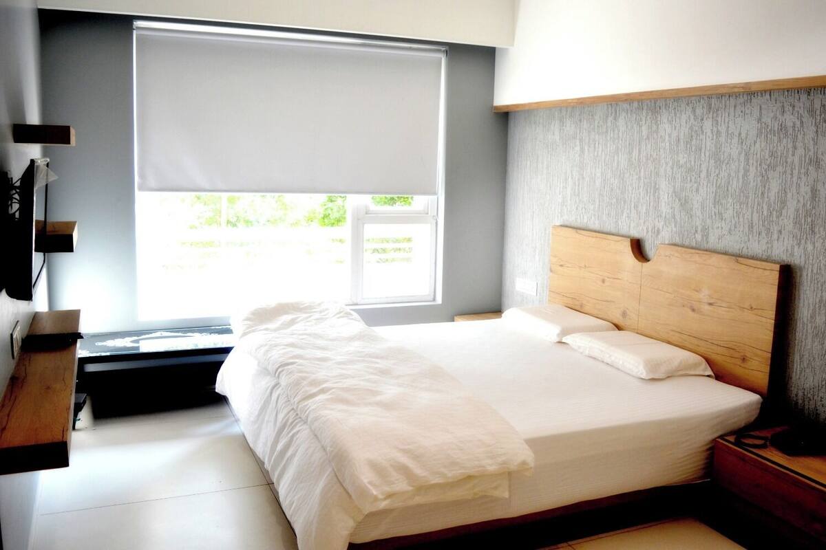 A bedroom with a bed, a wooden headboard, a window with blinds, and a grey textured wall.