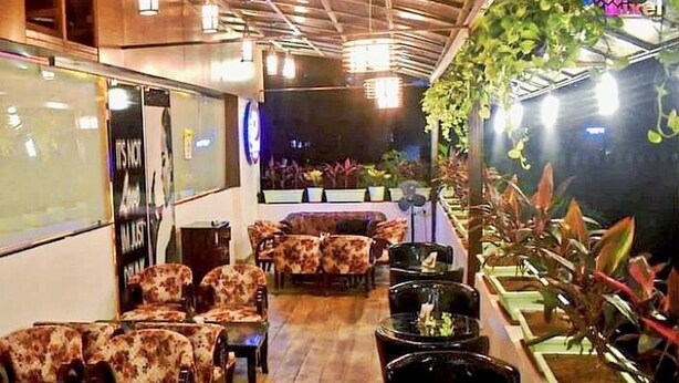 Un restaurante con una decoración moderna, que incluye sofás estampados, mesas redondas y una variedad de plantas.