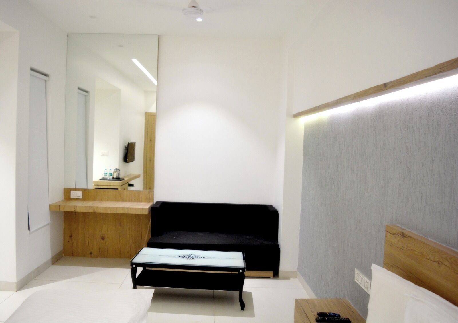 Quarto moderno e minimalista com um sofá preto, uma mesa de vidro pequena e um banco de madeira.