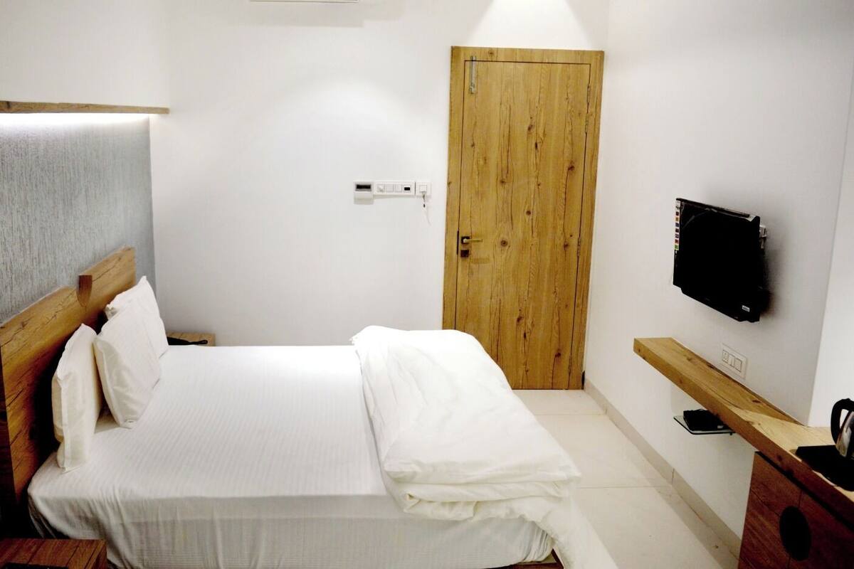 A bedroom with a bed, wooden headboard, a wooden door, a TV mounted on the wall, and a wooden bench.