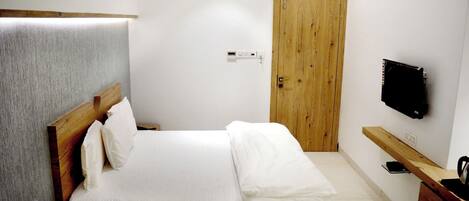 A bedroom with a bed, wooden headboard, a wooden door, a TV mounted on the wall, and a wooden bench.