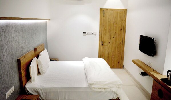 Un dormitorio con cama, cabecera de madera, una puerta de madera, televisor montado en la pared y un banco de madera.