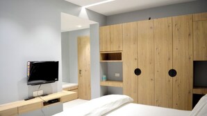 Un dormitorio moderno con cama, televisor y armario de madera con estantes.