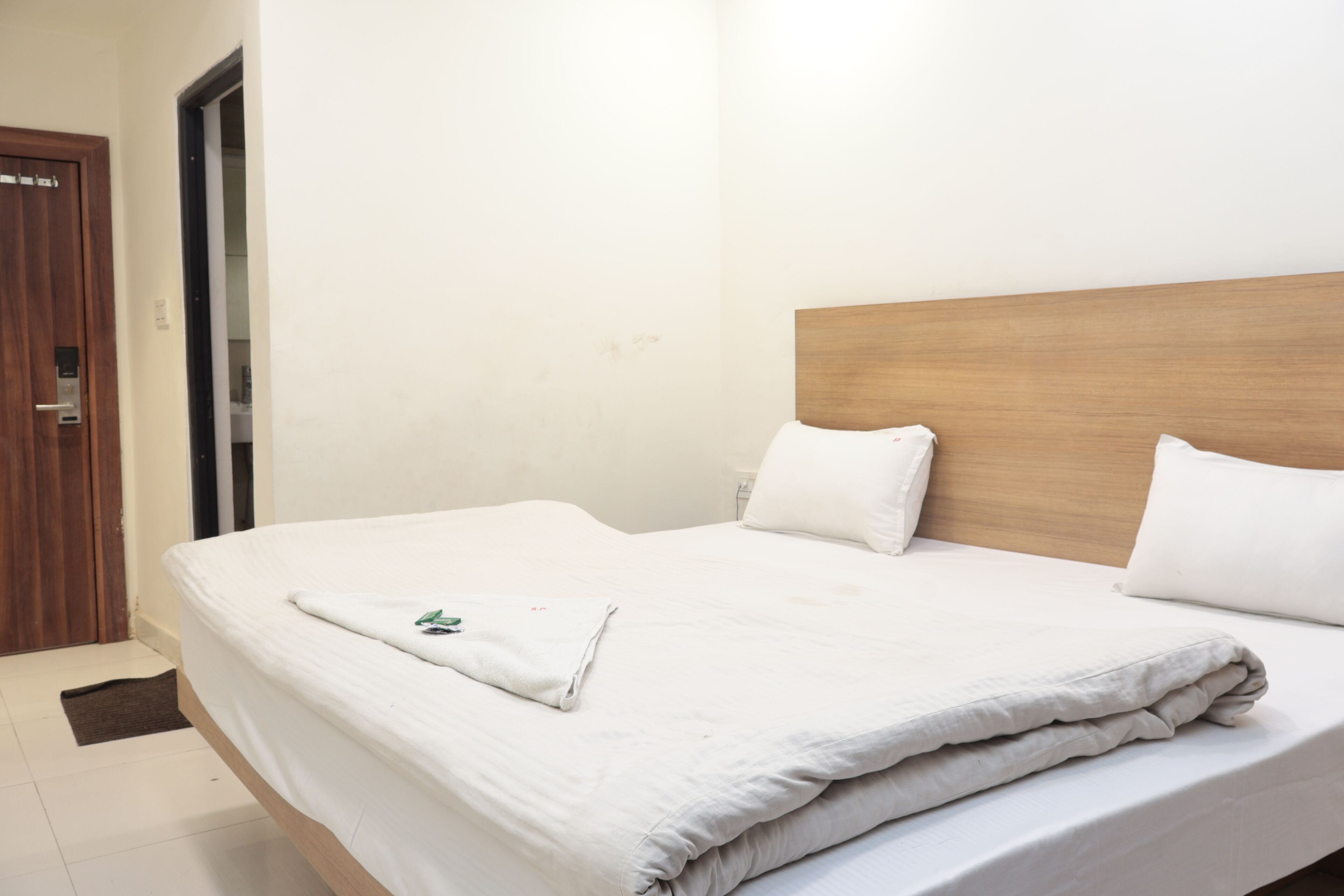 Una cama bien hecha con sábanas y almohadas blancas, un cabecero de madera y una puerta a la izquierda.