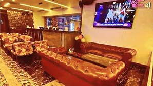 Un hall de hotel con un sofá rojo, alfombra estampada y una pantalla de televisión mostrando un programa.