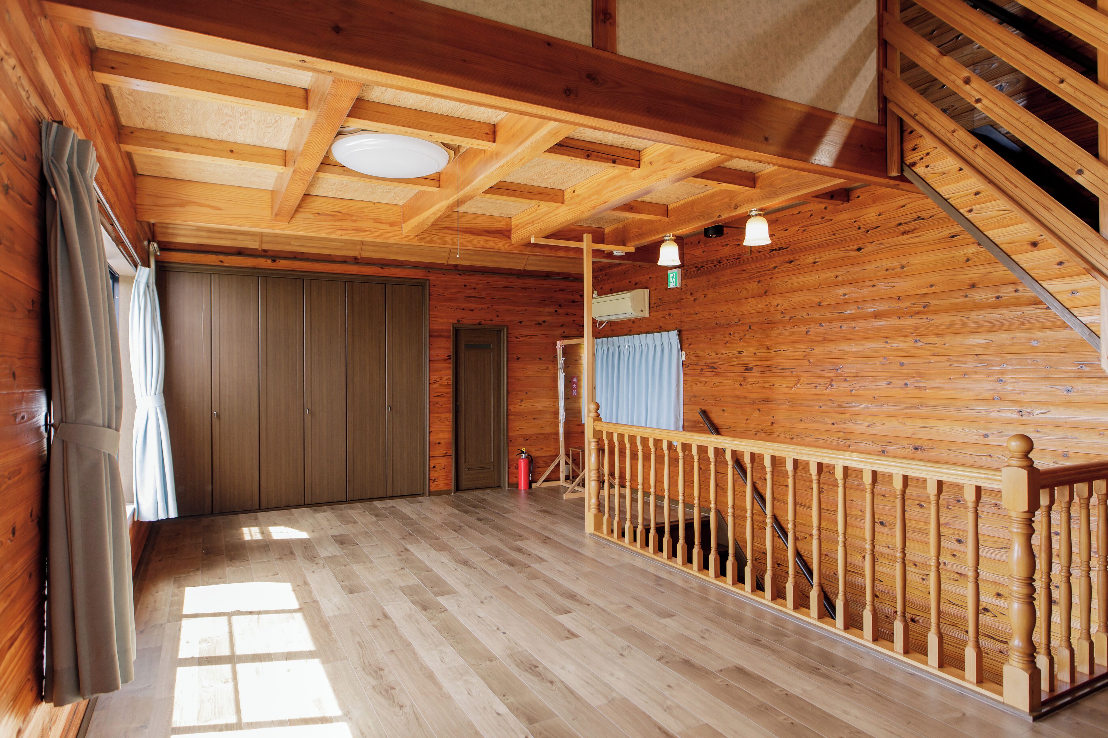 Un interior de madera con una escalera, piso de madera y techo con vigas a la vista.