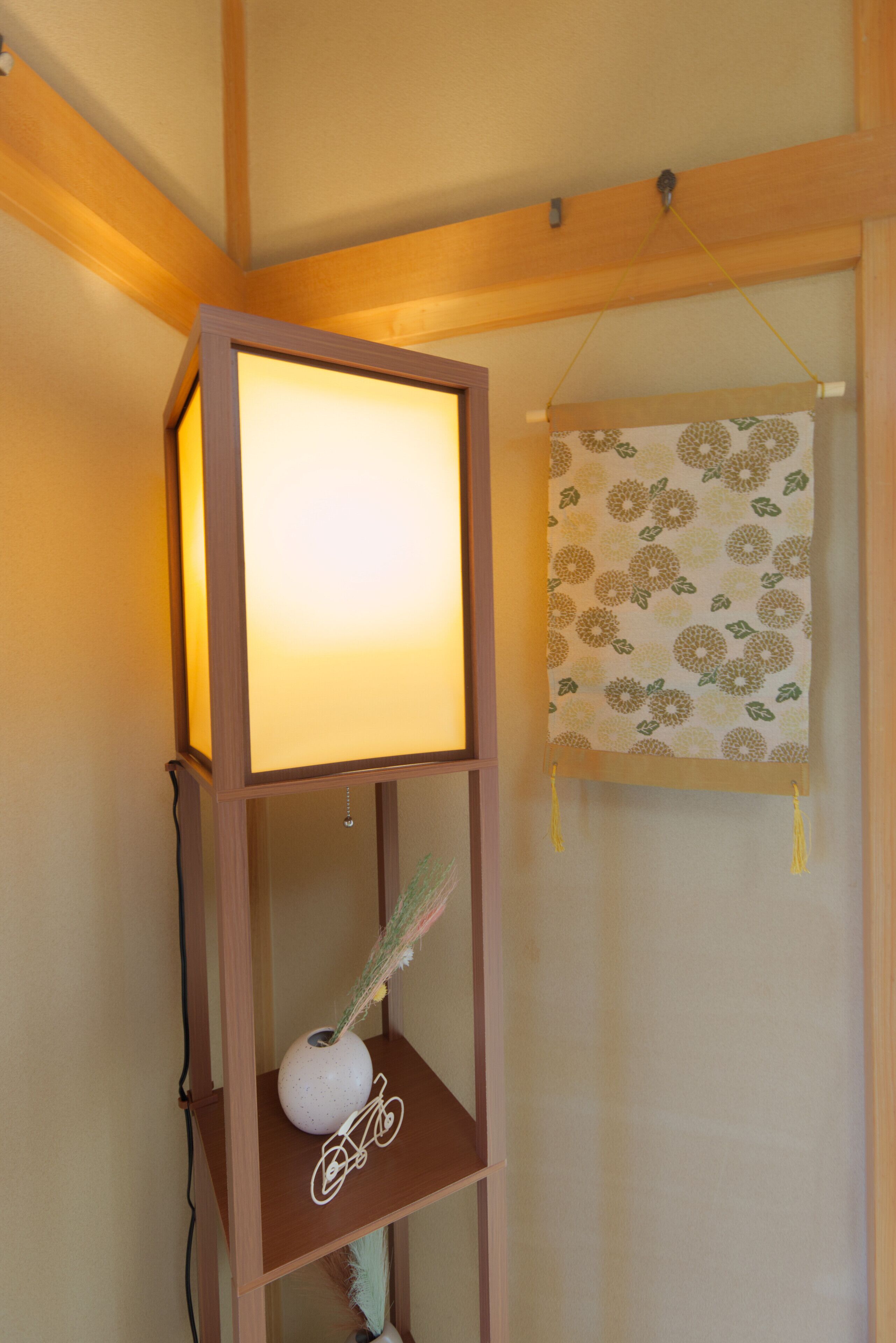 A wooden shelf with a lit lamp, a decorative vase, and a hanging patterned cloth.