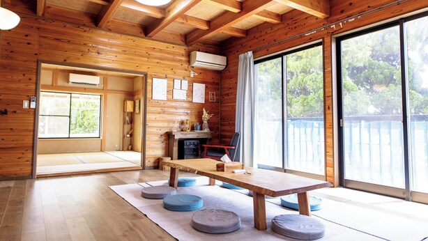 Un intérieur en bois avec des tatamis, une table à manger en bois et une porte-fenêtre coulissante donnant sur une terrasse.