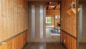 Un couloir intérieur en bois, avec une porte coulissante donnant sur une pièce où se trouvent un tatami et une petite table.