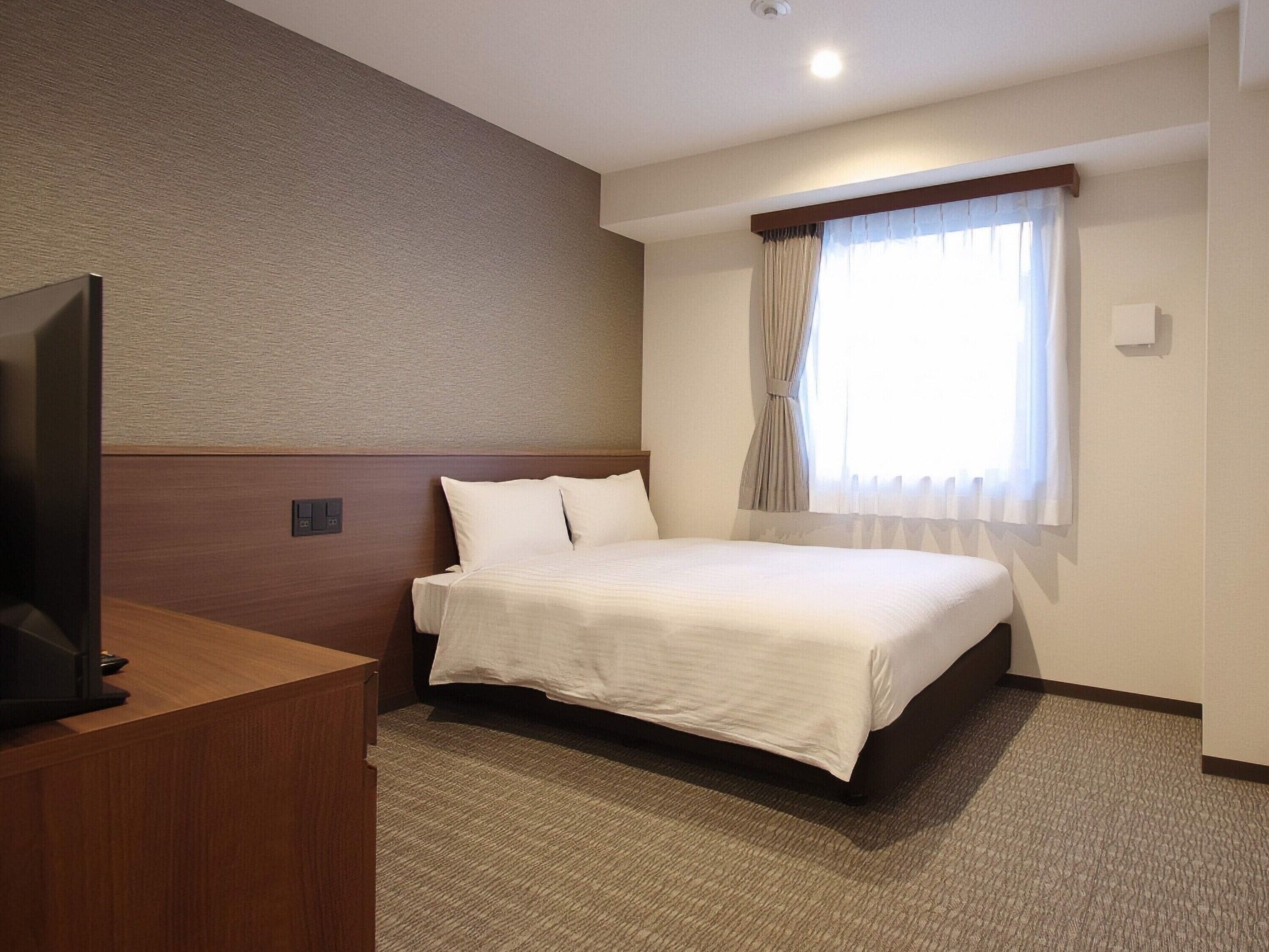 Ein Hotelzimmer mit einem Bett, einem Fernseher auf einem Holztisch und einem Fenster mit Vorhängen.