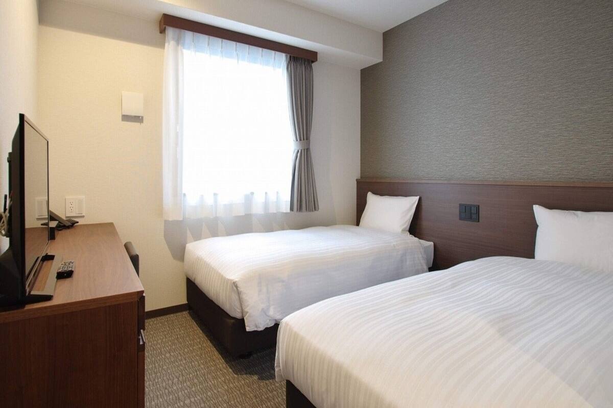 Habitación de hotel con dos camas, un escritorio con computadora y una ventana con cortinas.