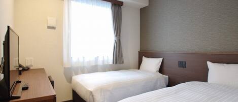 A hotel room with two beds, a desk with a computer, and a window with curtains.
