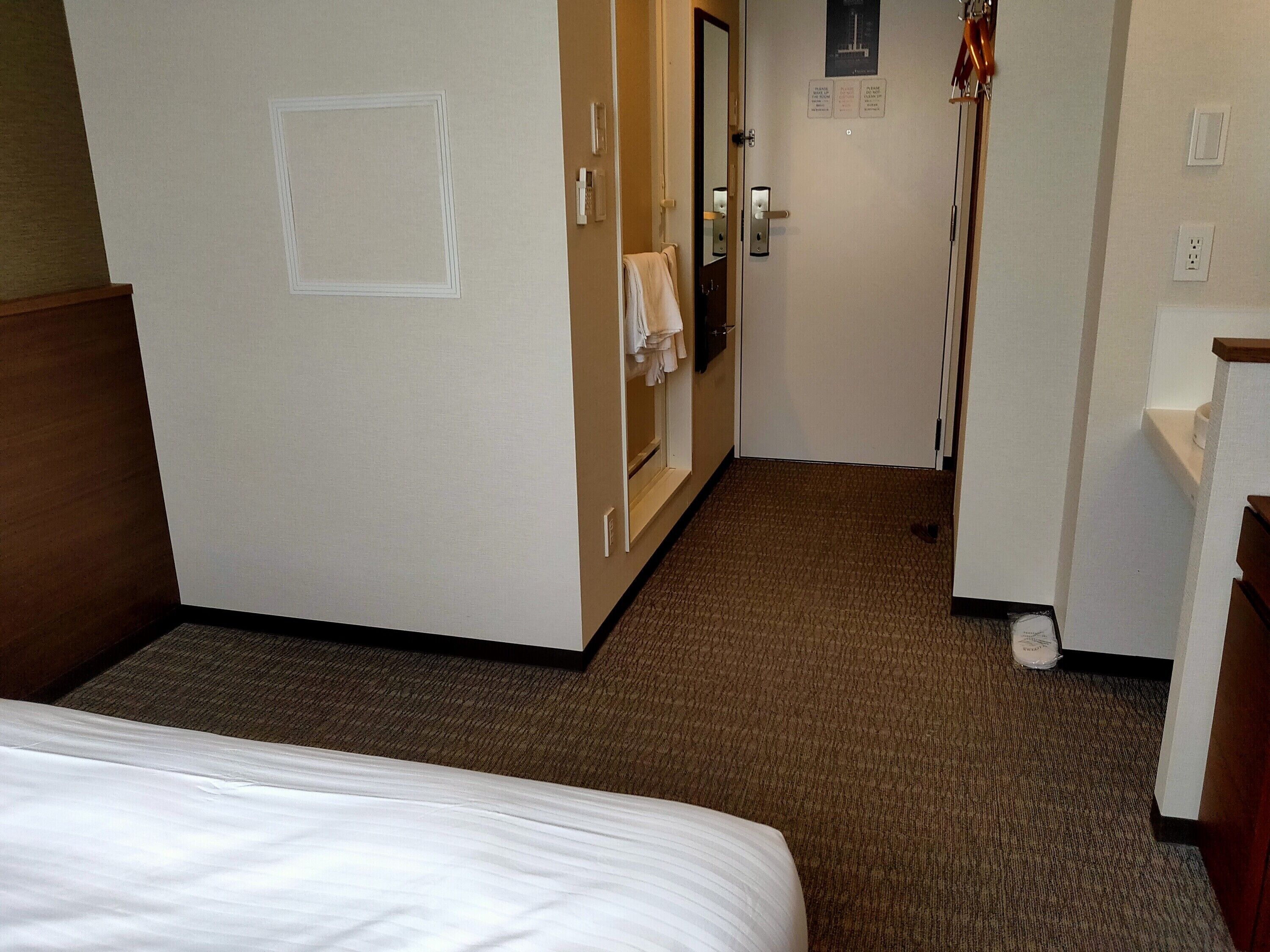 A hotel room with a bed, a door, a mirror, a towel rack, and a carpeted floor.