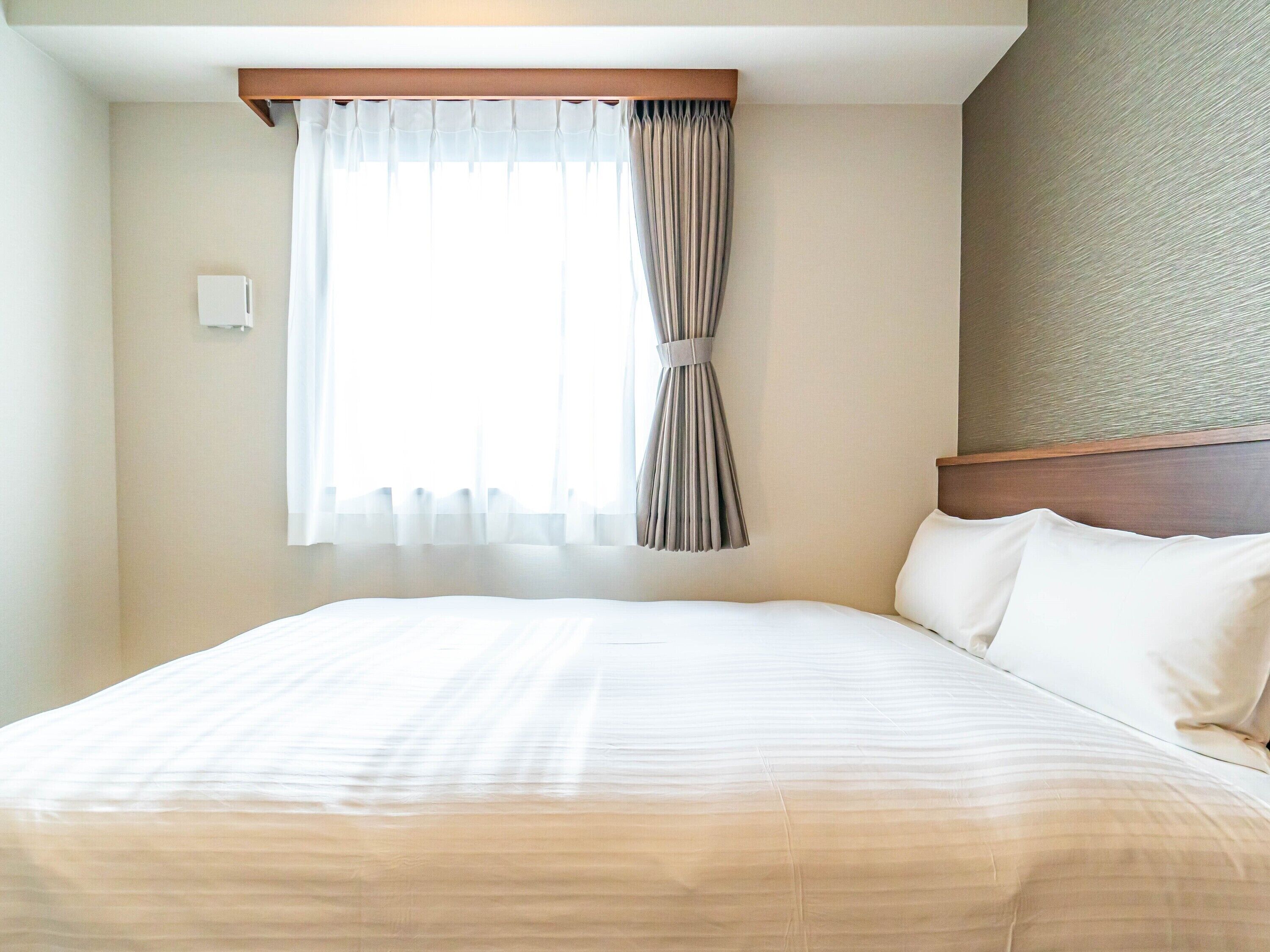 A hotel room with a large bed, a window with curtains, and a textured wall.