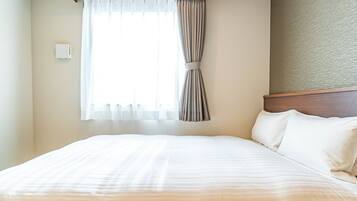 A hotel room with a large bed, a window with curtains, and a textured wall.