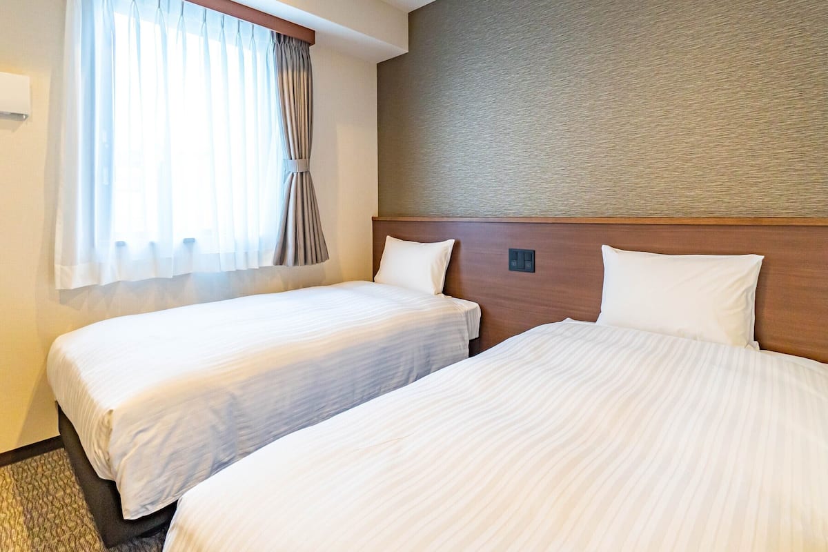 Una habitación de hotel con dos camas, una ventana con cortinas y una pared con textura.
