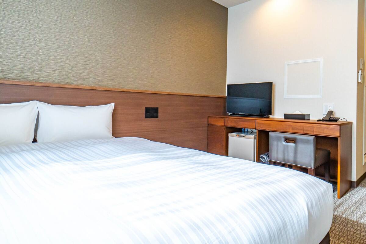 Una habitación de hotel con una cama grande, un escritorio con televisor y un refrigerador pequeño.