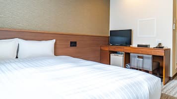 A hotel room with a large bed, a desk with a television, and a small refrigerator.
