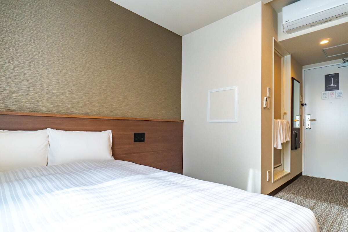 Una habitación de hotel con una cama grande, un cabecero de madera, un aire acondicionado de pared y una puerta que da al baño.