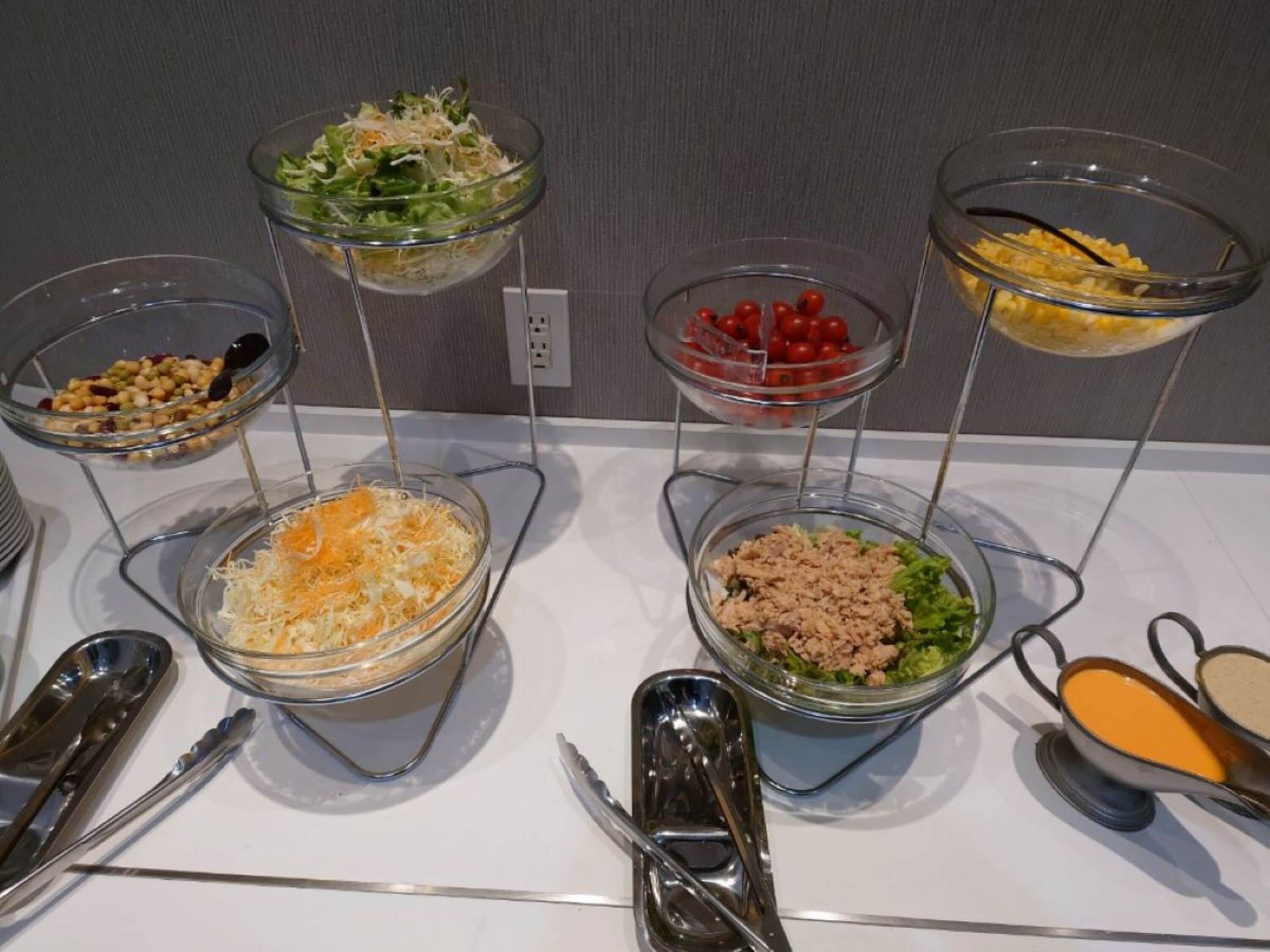 A buffet table with various food items in clear bowls, utensils, and a condiment container.