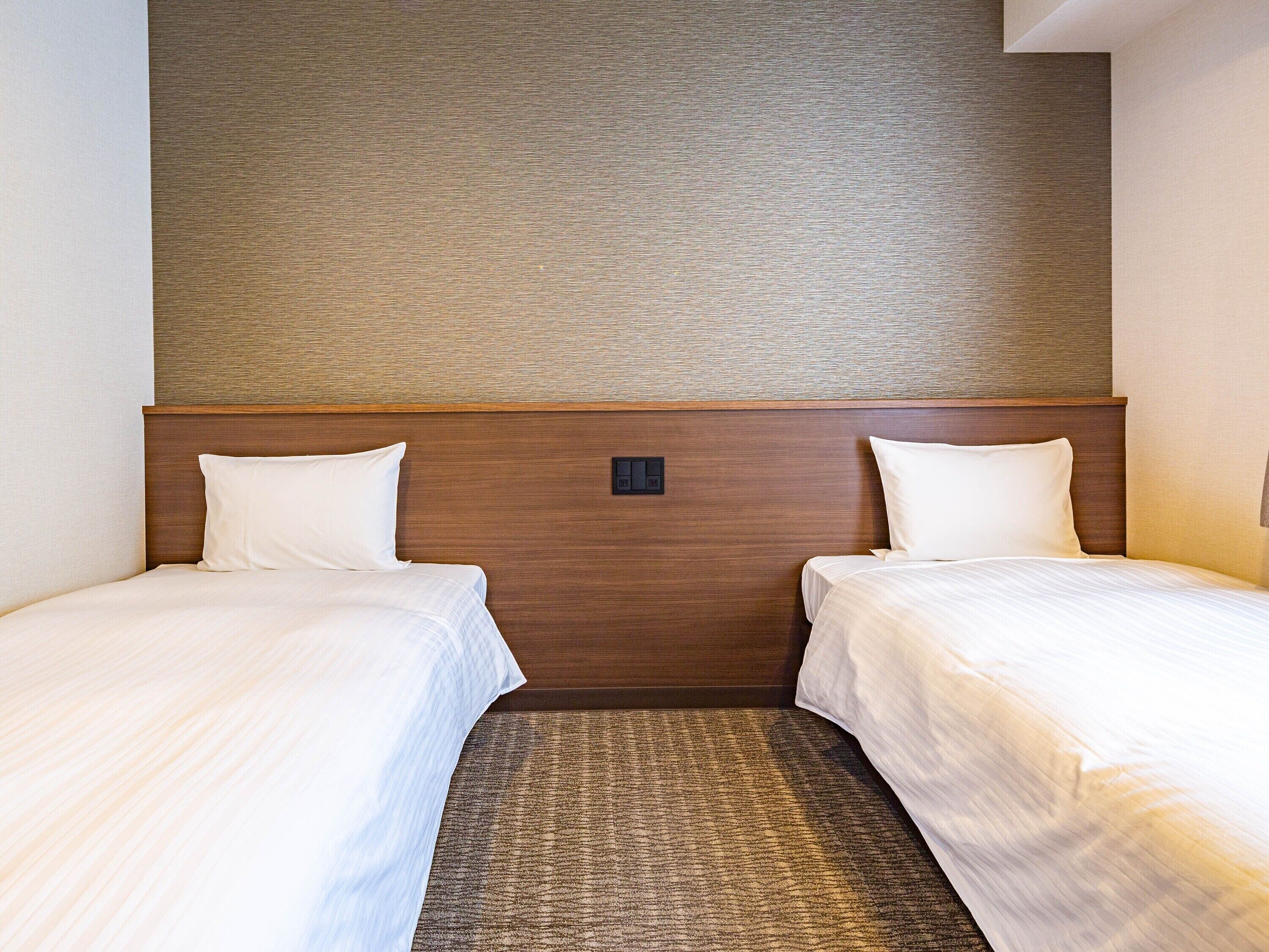A hotel room with two single beds, a wooden headboard, and a textured wall.
