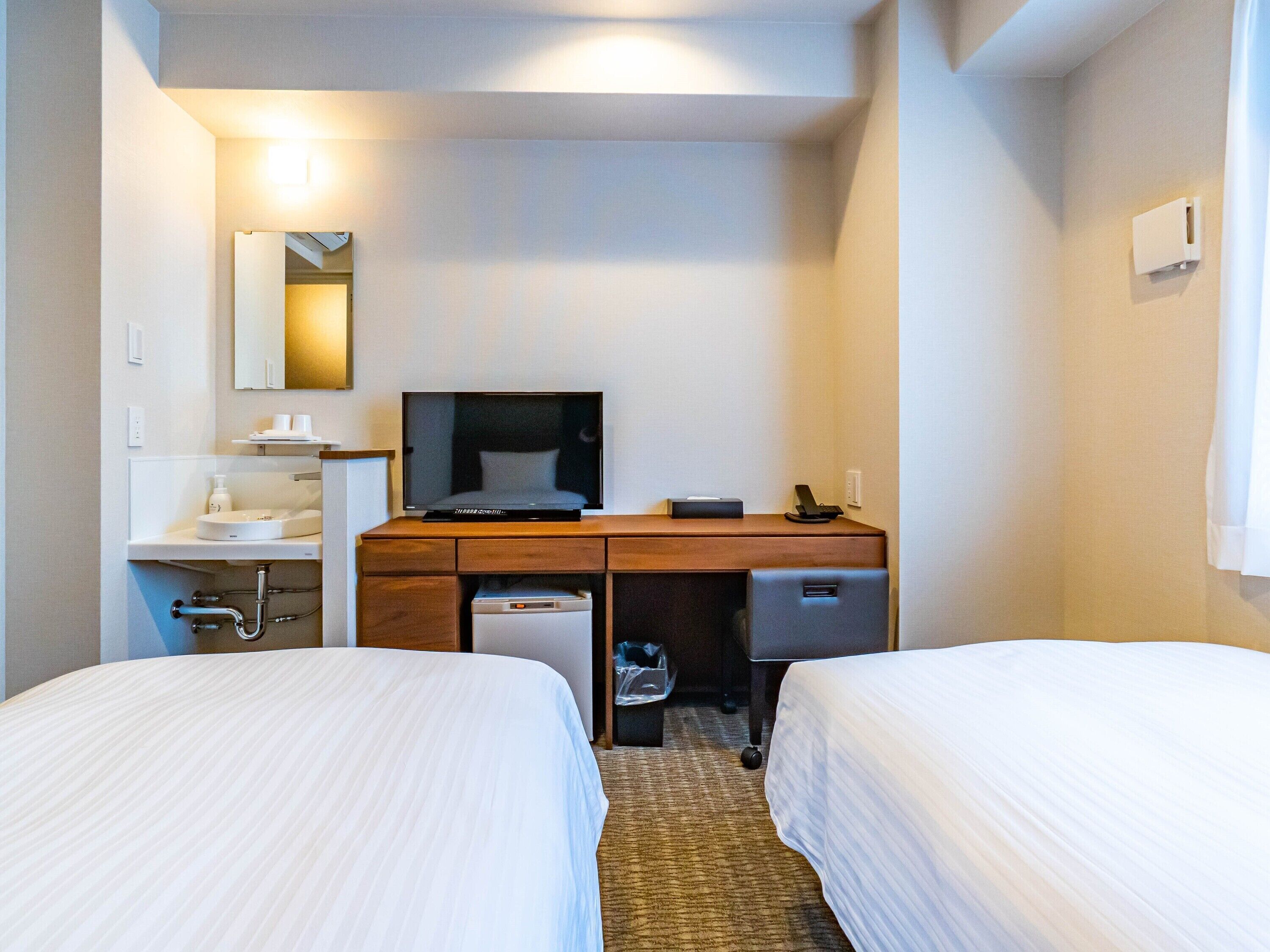 Une chambre d’hôtel avec deux lits, un bureau doté d’un téléviseur à écran plat, un petit lavabo et un miroir.