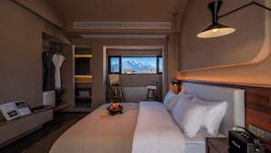 A hotel room with a large bed, a bedside table with a radio, a window with a mountain view, a small stool, and a bookshelf with books and a plant. - XIU YU Villa (Lijiang)