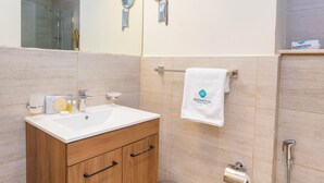 A bathroom with a wooden vanity, a white sink, two wall-mounted mirrors, a towel rack with a white towel, and a shower area.
