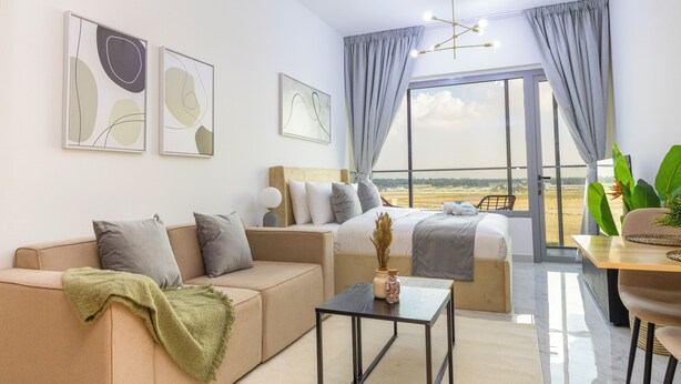 A modern hotel room with a sofa, a bed, a dining table, and a view of the beach.