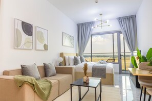 A modern hotel room with a sofa, a bed, a dining table, and a view of the beach.