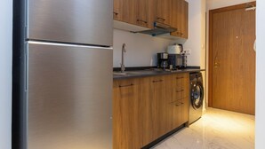 A compact kitchen with wooden cabinets, a stainless steel refrigerator, a coffee maker, and a washing machine.