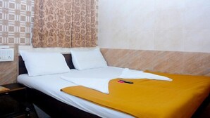 Una cama bien hecha con ropa de cama blanca y amarilla, una cortina estampada y una pared de azulejos.