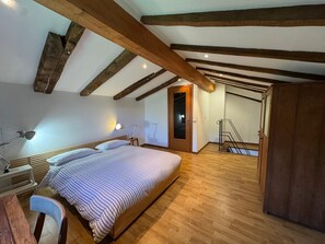 A bedroom with a wooden ceiling, a bed, a desk, and a chair.