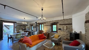 A spacious living area with a sofa, armchairs, a coffee table, and a kitchen in the background.