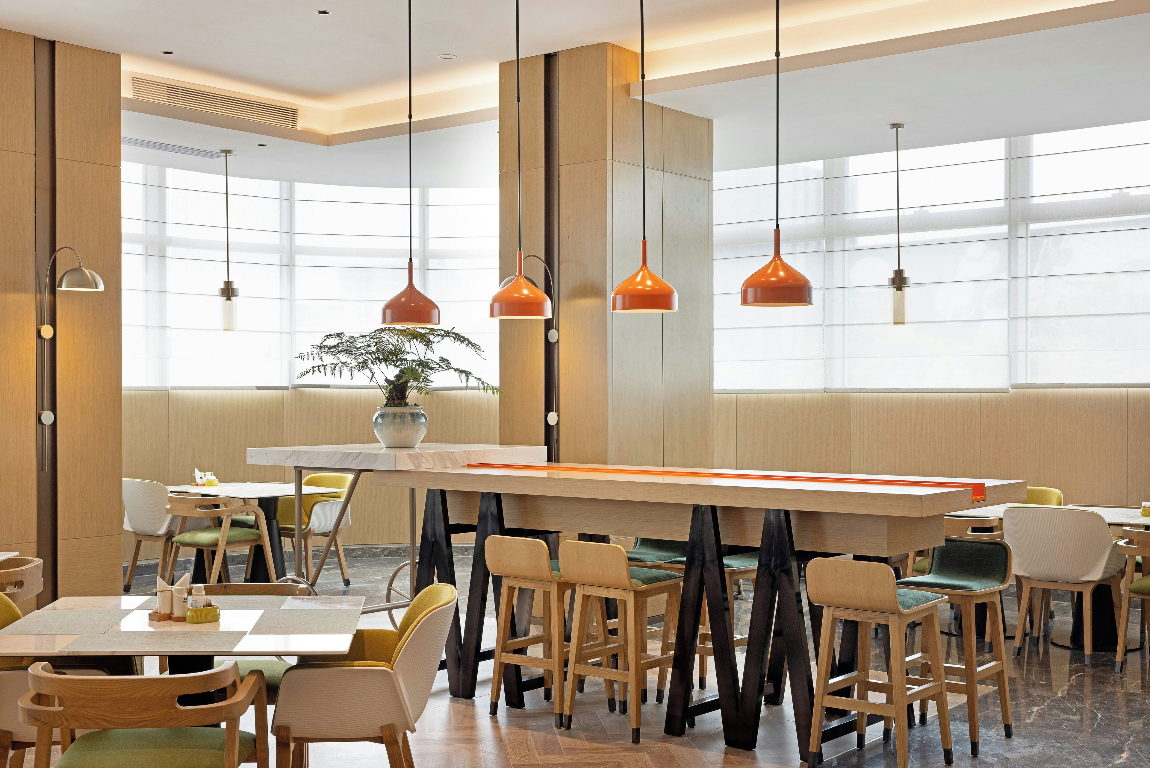 A modern dining area with wooden furniture, pendant lighting, and large windows.