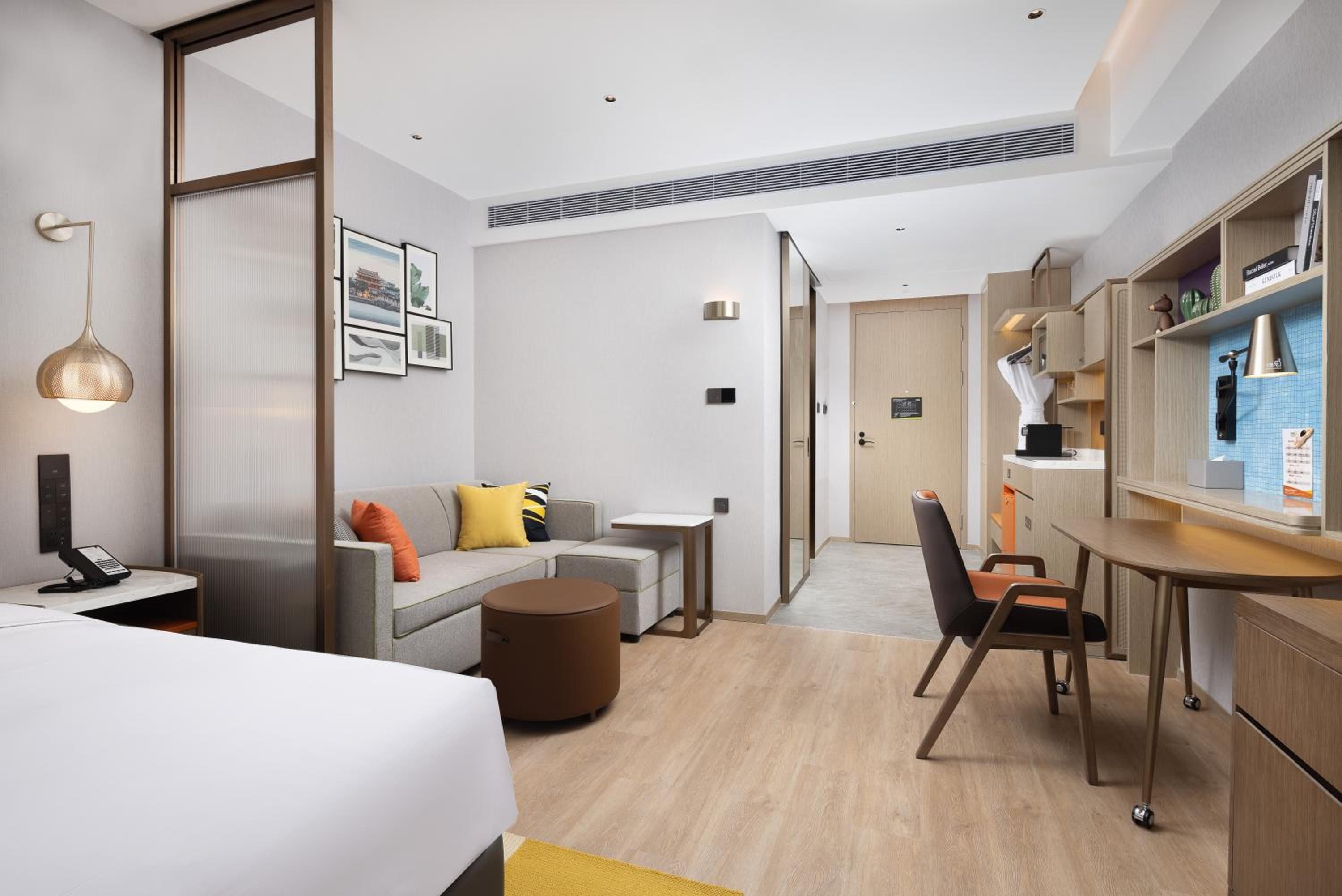 A modern hotel room with a bed, a desk, a sofa, and a dining area.