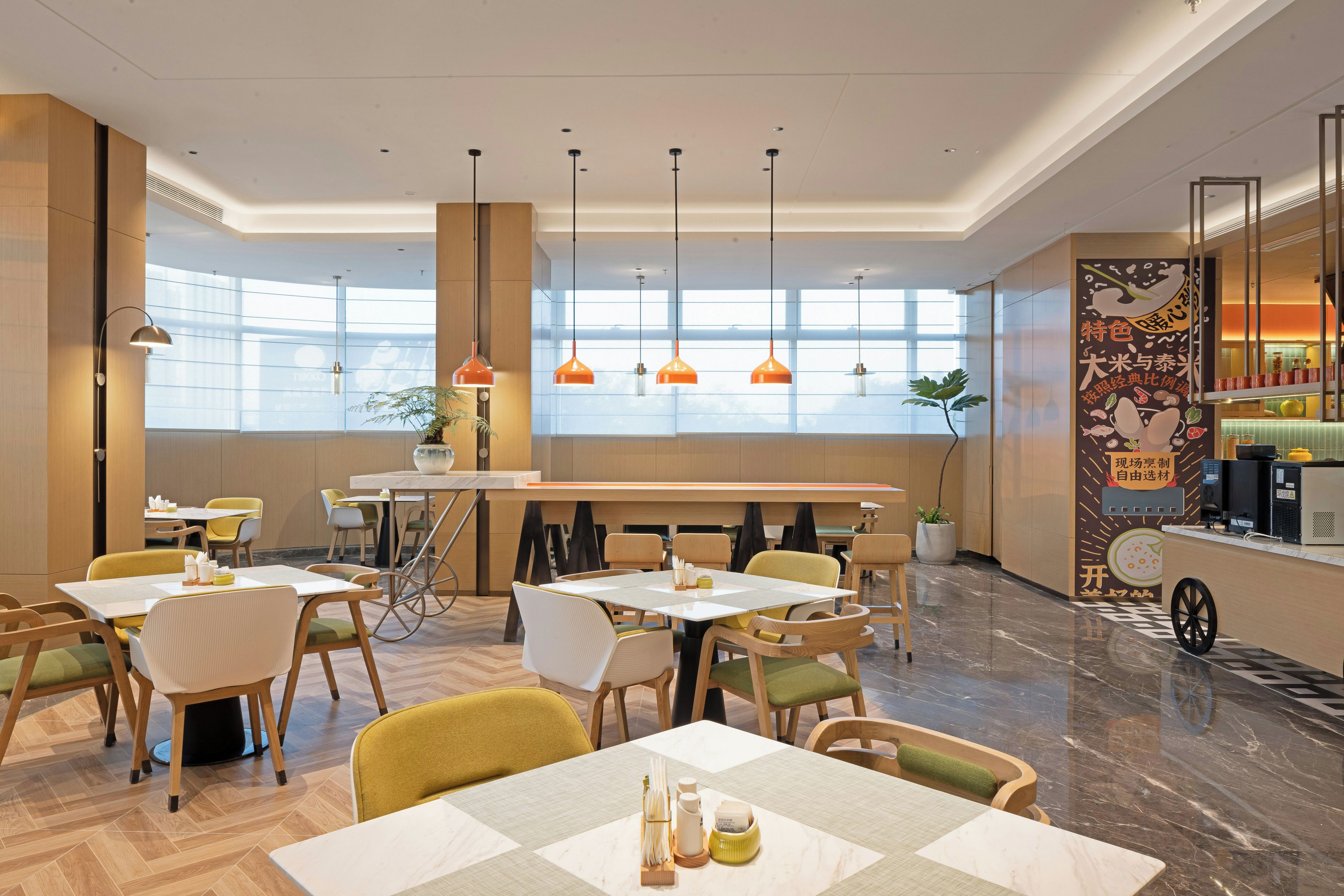 A modern dining area with tables and chairs, pendant lighting, and large windows.