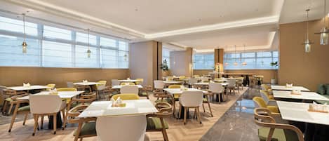 A spacious dining area with multiple tables and chairs, large windows, and a modern ceiling design.