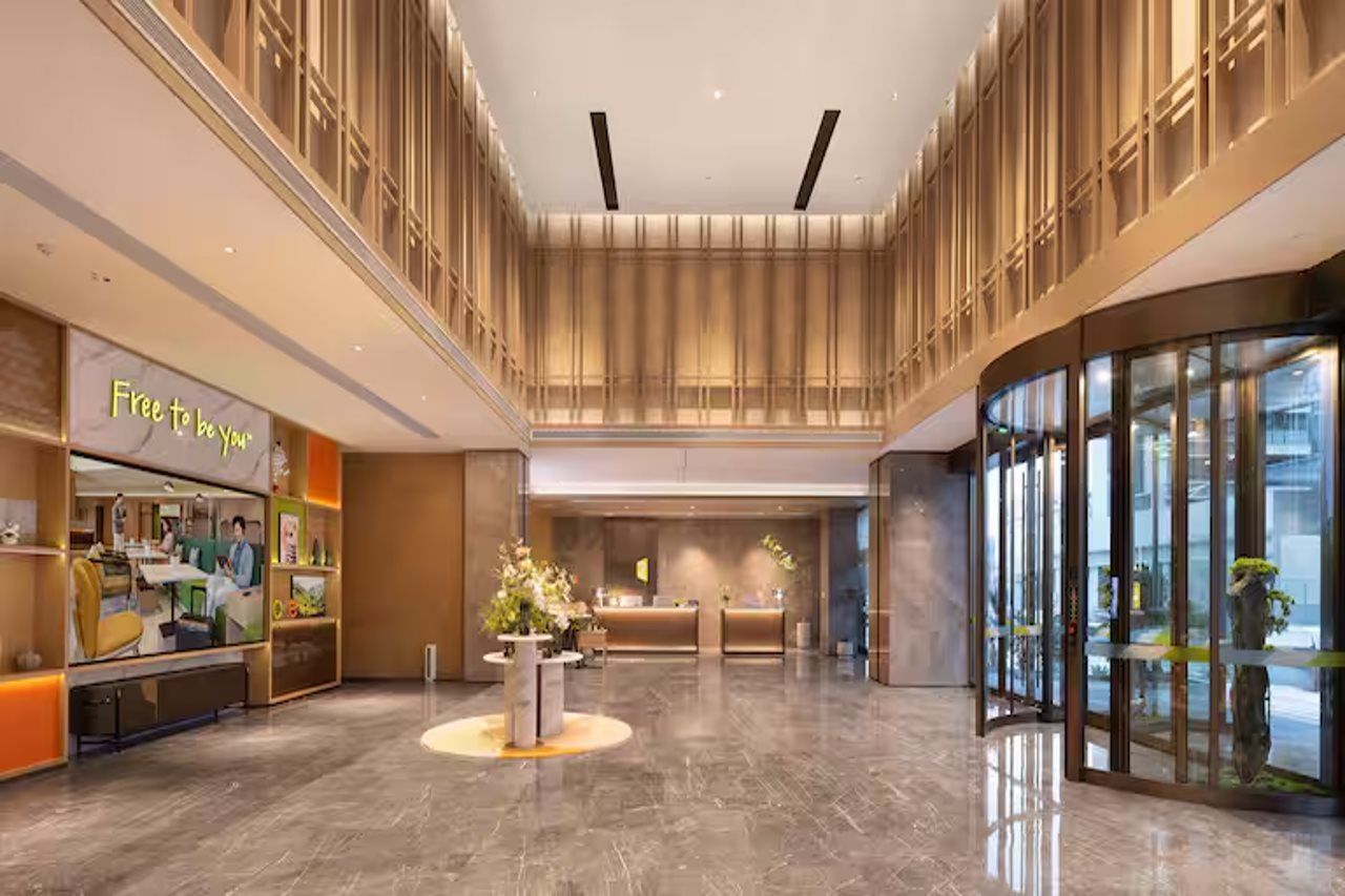 A modern hotel lobby with a reception desk, a seating area, and a glass entrance.