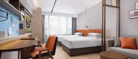 Habitación de hotel moderna con una cama, un escritorio, una silla, un sofá y un pequeño reposapiés.