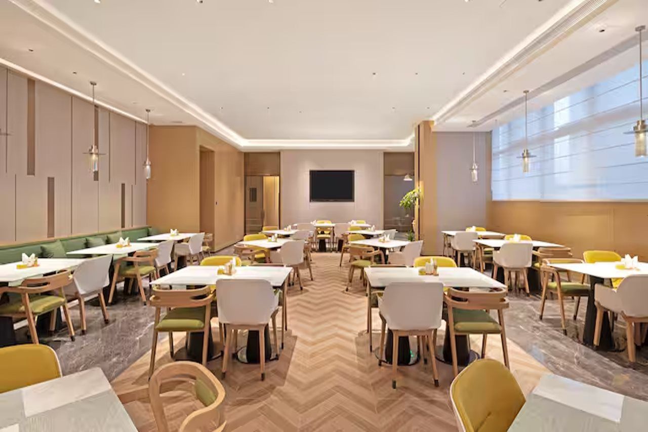 Un espace de restauration d’hôtel comprenant plusieurs tables et chaises, un téléviseur à écran plat fixé au mur et un sol décoré d’un motif en chevrons.