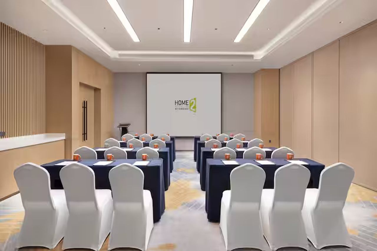 A conference room with a presentation screen, tables, and chairs arranged for a meeting.