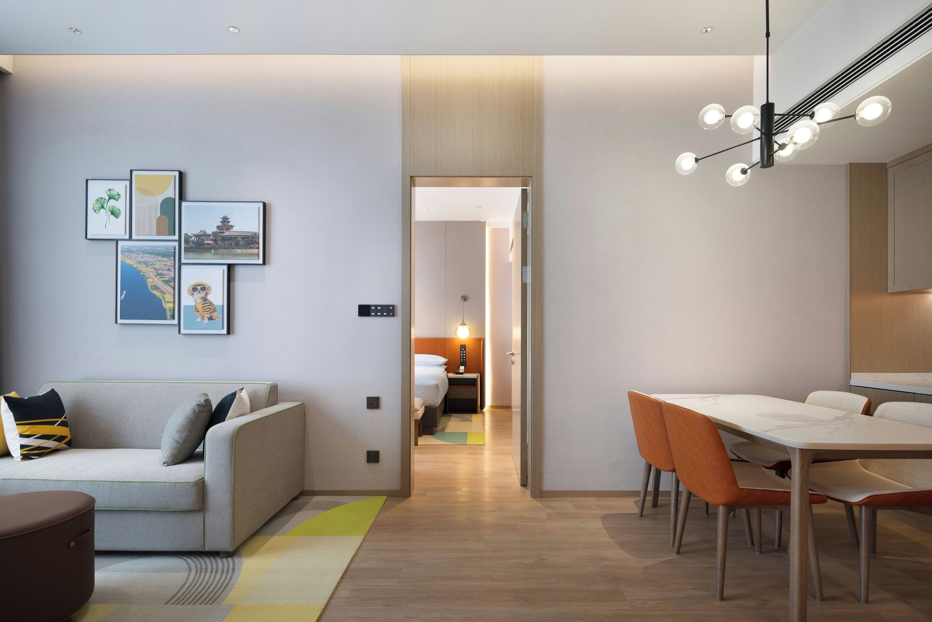 Une chambre d’hôtel moderne comprenant un canapé, une table à manger avec des chaises, un couloir menant à une autre pièce et des œuvres d’art accrochées au mur.