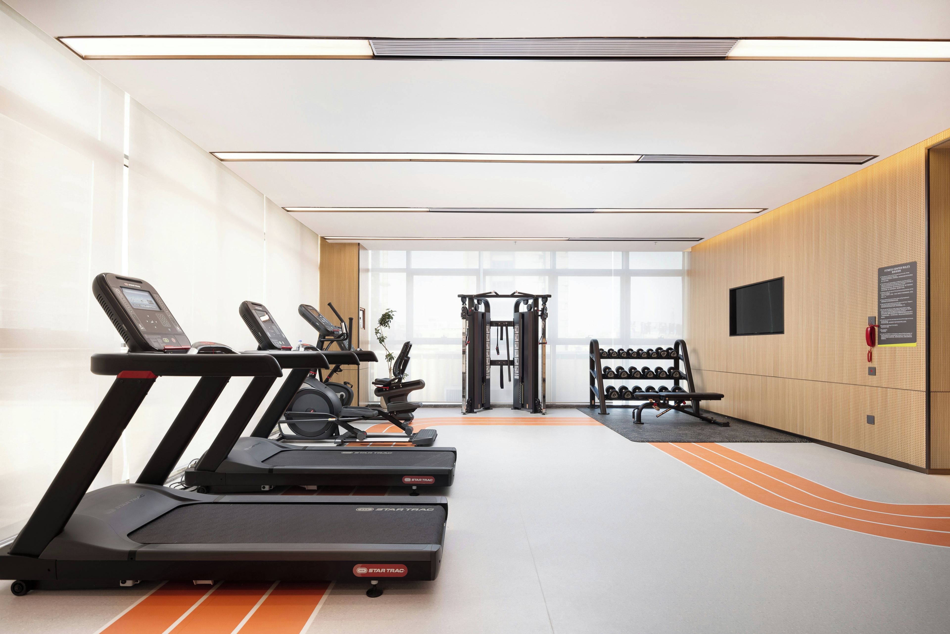 Un gimnasio con cintas de correr, máquinas de pesas y un televisor montado en la pared.