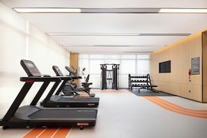 A gym with treadmills, weight machines, and a wall-mounted TV.
