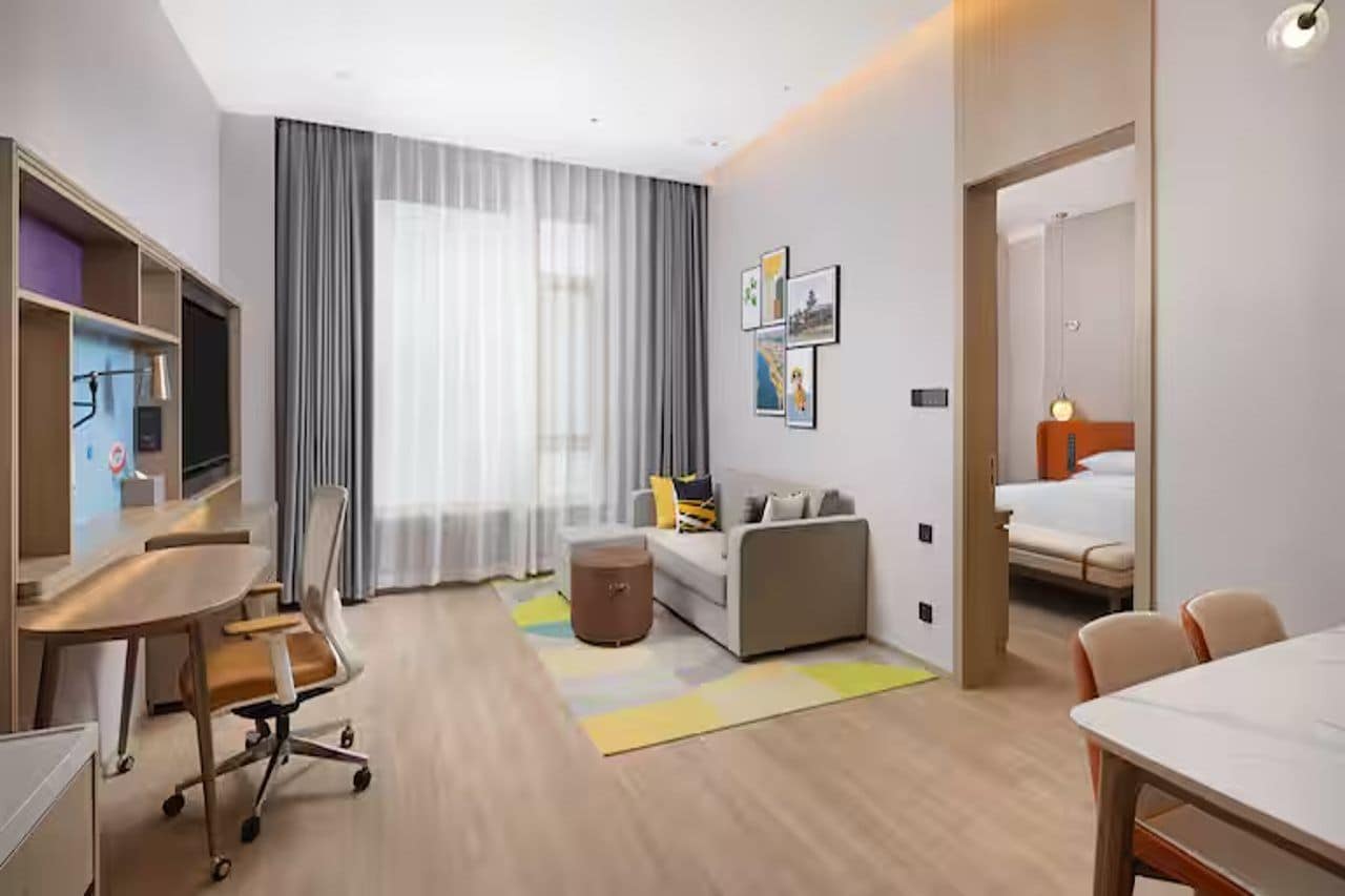A modern hotel room with a desk, sofa, and bed.