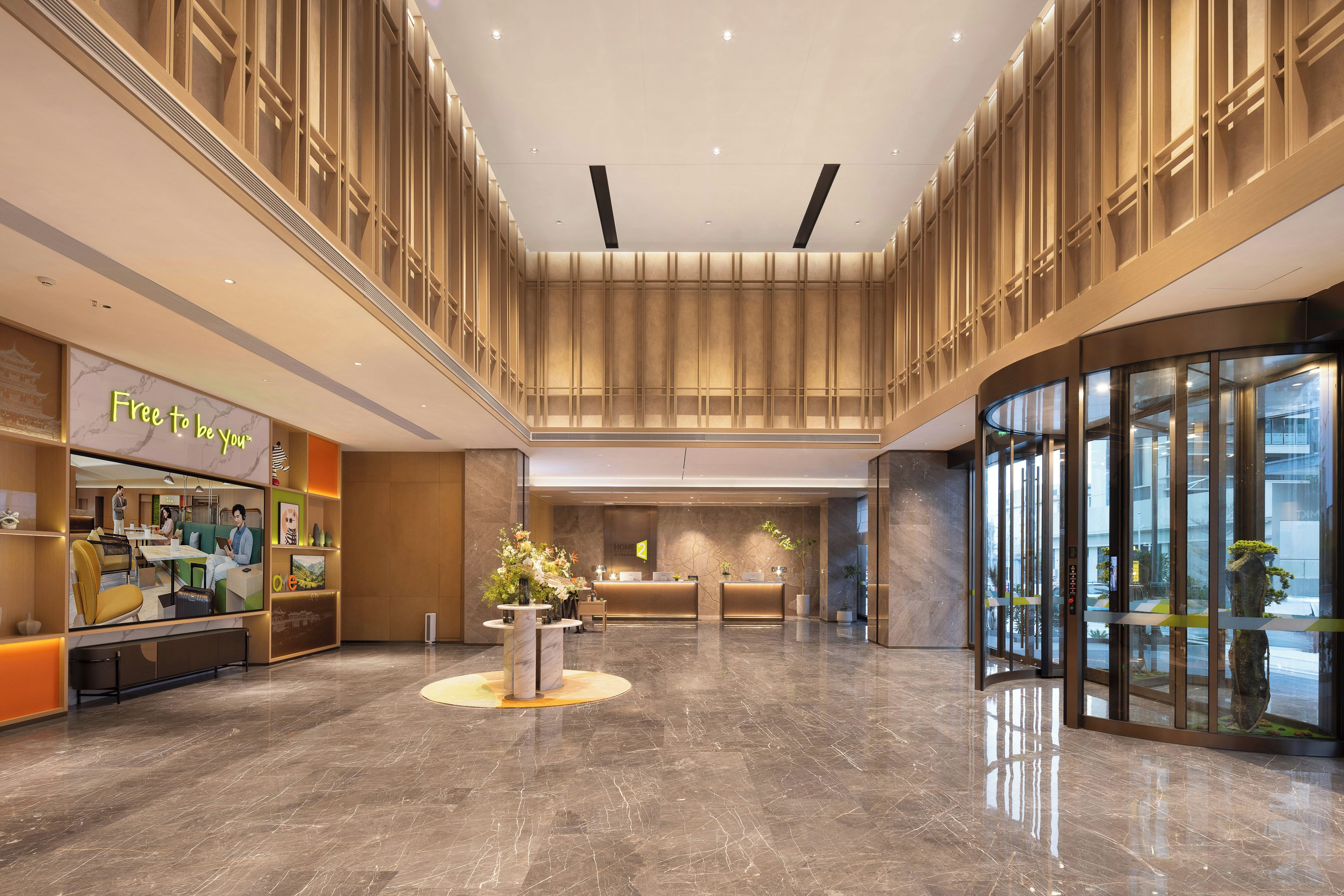 A hotel lobby with a reception desk, seating area, and a glass elevator.