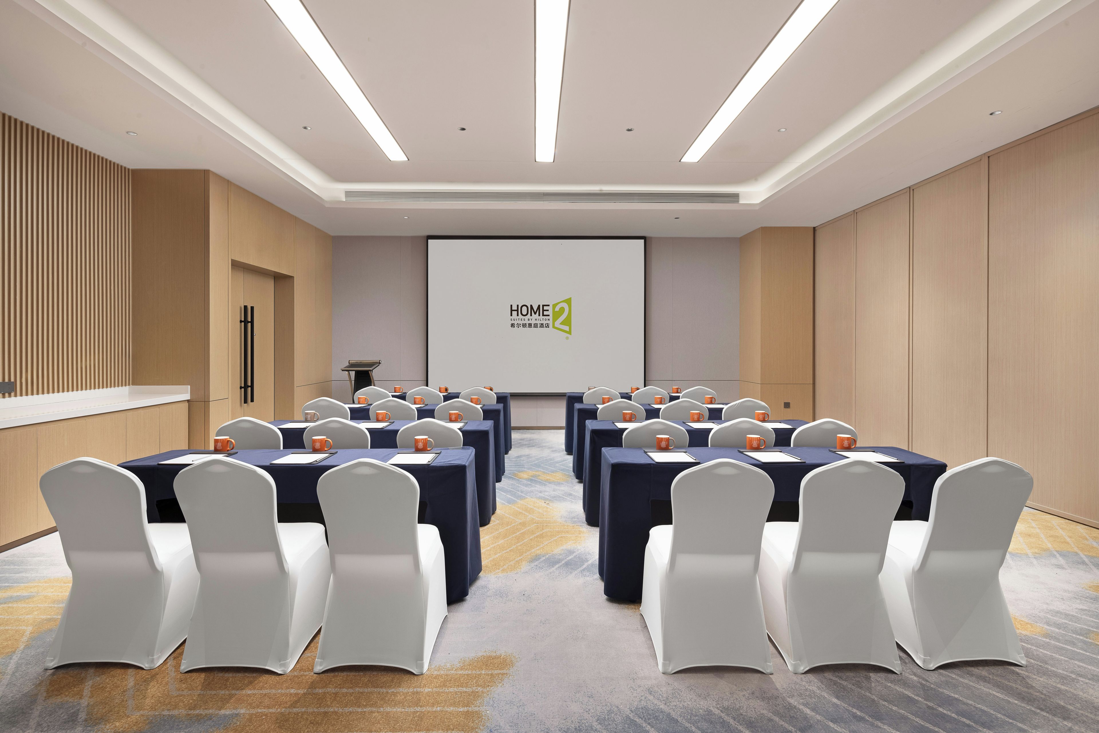 A conference room with tables, chairs, and a presentation screen.