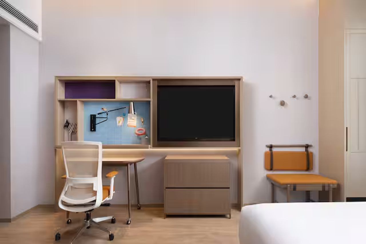 A hotel room with a bed, a desk with a computer, a chair, and a small table.