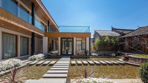 En modern byggnad med en entré av glas, en innergård med stenplattor och traditionell arkitektur i bakgrunden.
